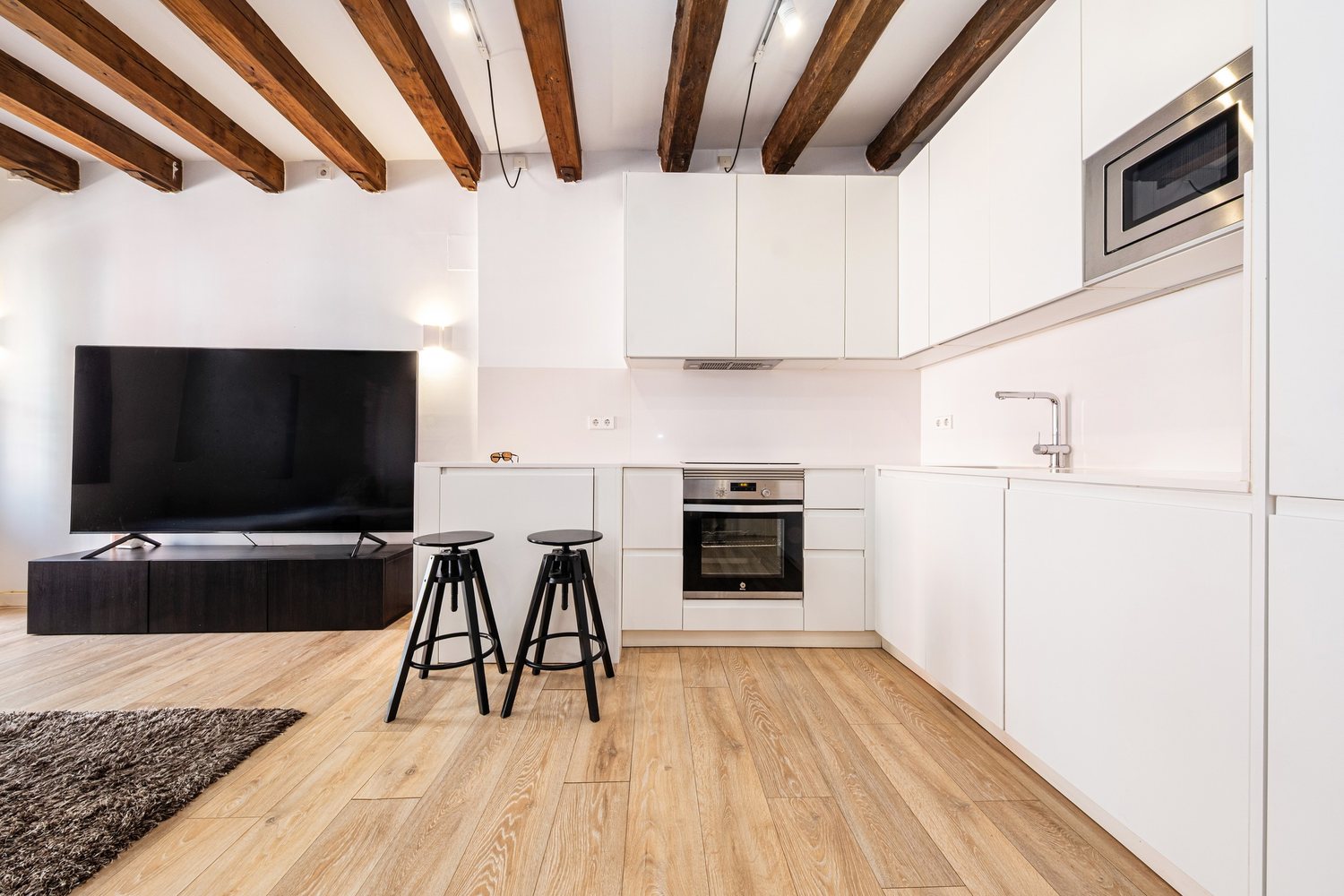 Open-plan white kitchen with breakfast stools under timber beams