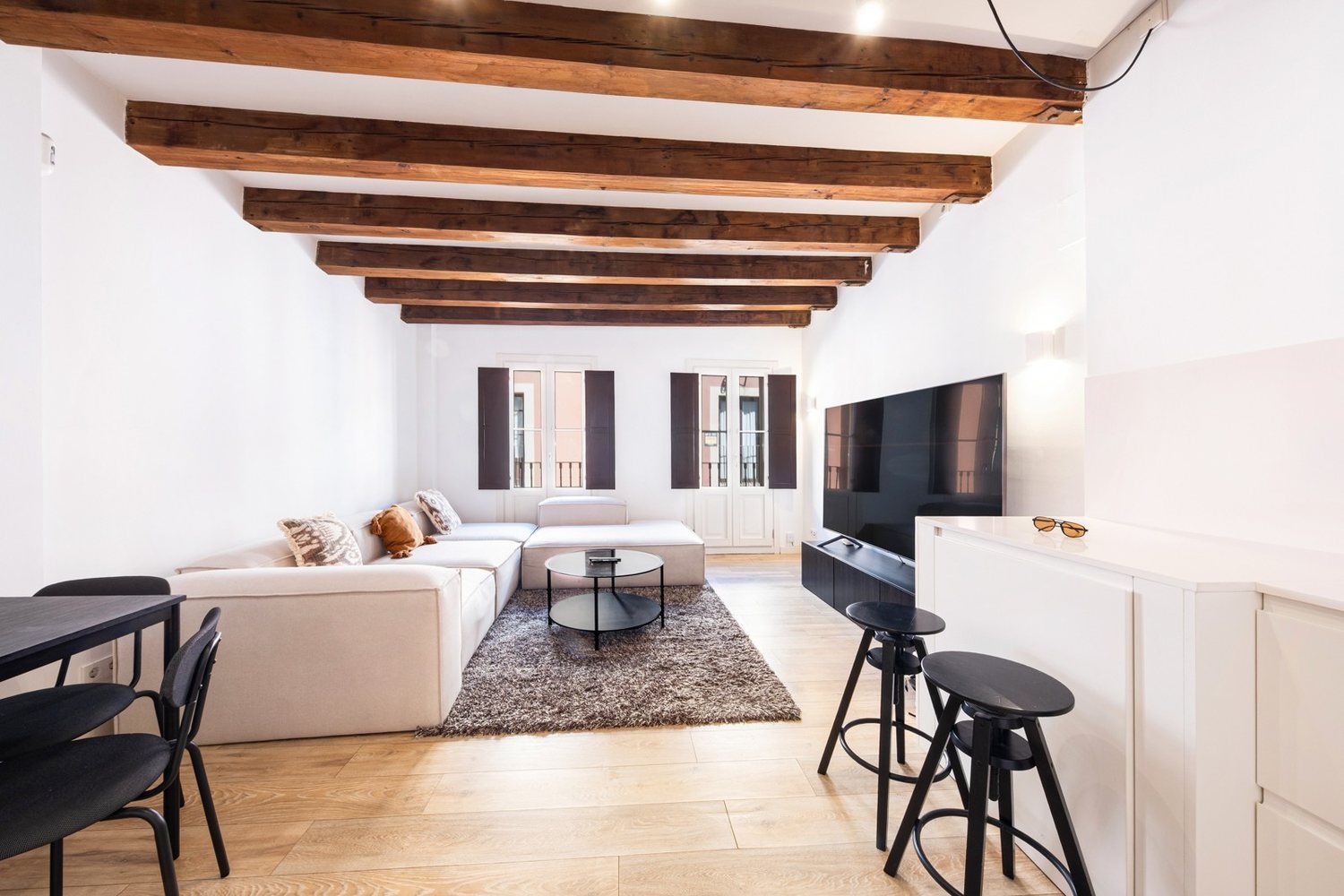 Living room with original timber beams, corner sofa and shuttered balcony doors